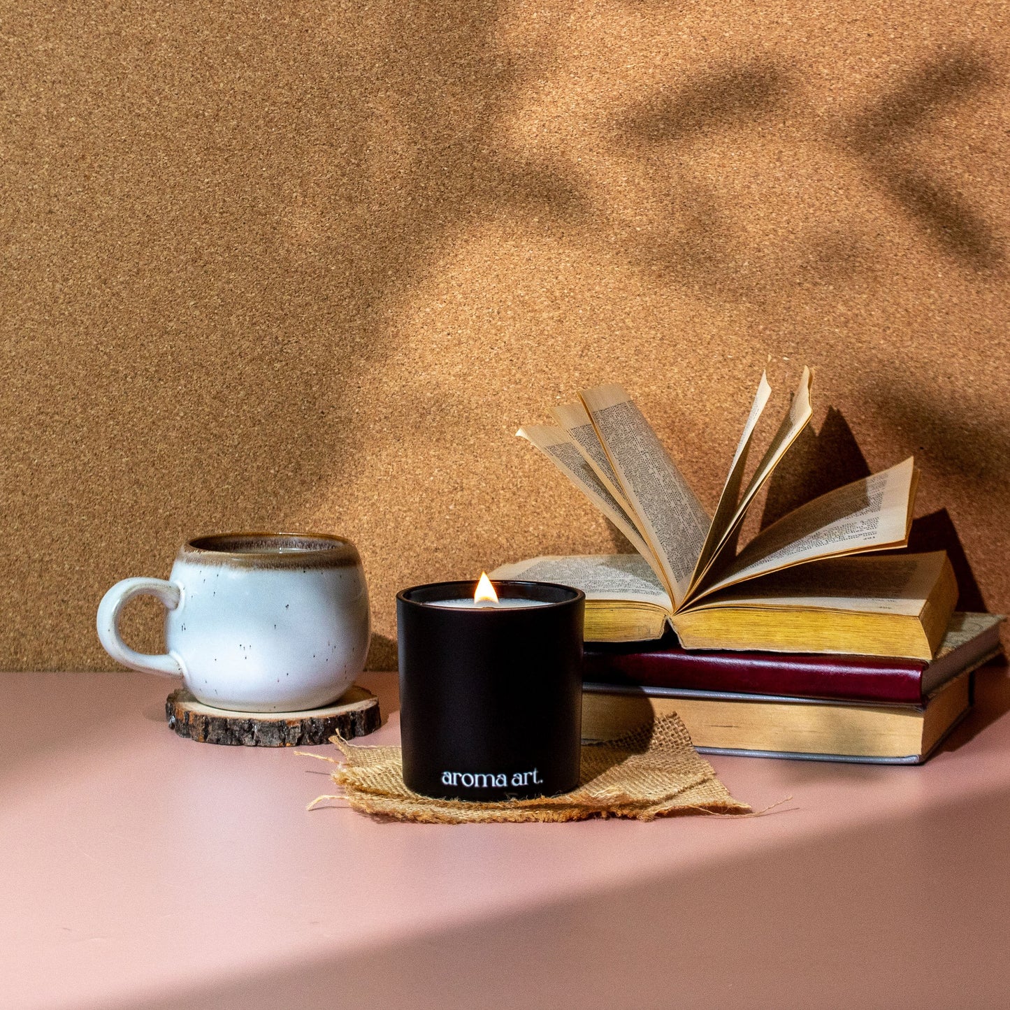 7oz crackling wooden wick soy coconut wax candle named Dark Academia, with notes of cardamon, leather, and cedar. A mysterious and elegant scent perfect for a night in with a good book. Shown with a cozy mug of tea and a stack of vintage books.