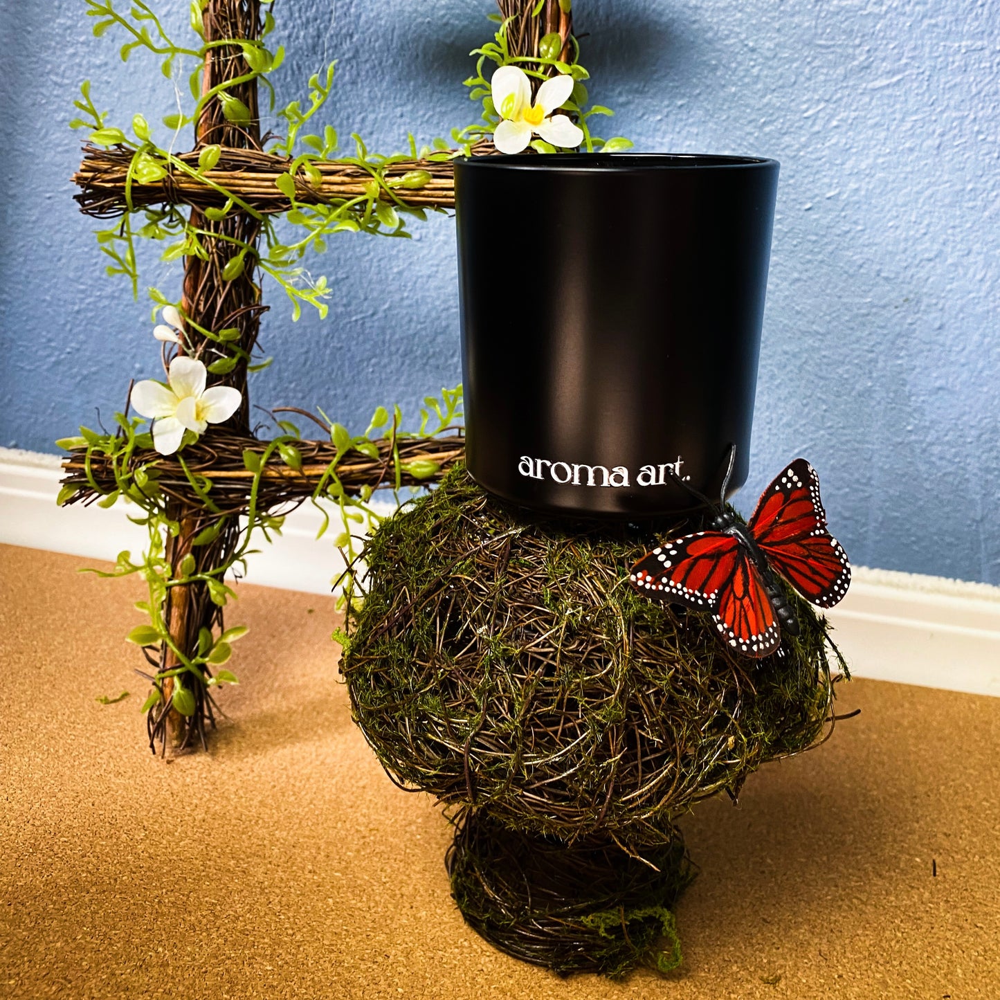 7 oz Herb Garden crackling wooden wick candle with notes of herbs, basil, and mint. Shown in its elegant black vessel, shown atop a sweet mushroom made of moss and branches. A fresh and verdant candle perfect for spring.