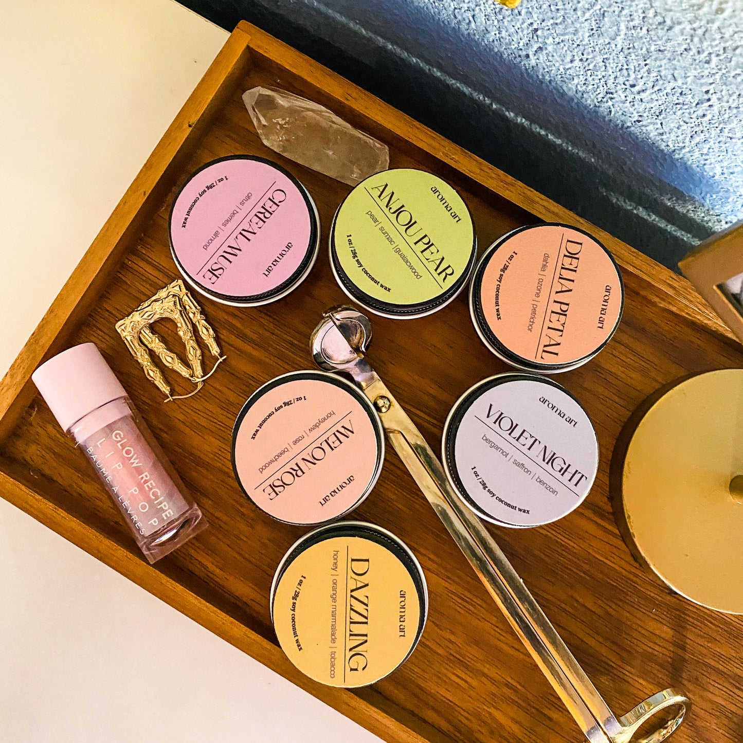 Luxuriously arranged on a wooden tray are six candles in travel size tins in a variety of scents, evoking a sense of a self-care day. The scents are (from left to right), Cereal Muse, Melon Rose, Dazzling, Anjou Pear, Delia Petal, and Violet Night.